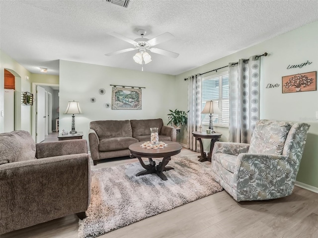 living area featuring visible vents, ceiling fan, light wood finished floors, and a textured ceiling