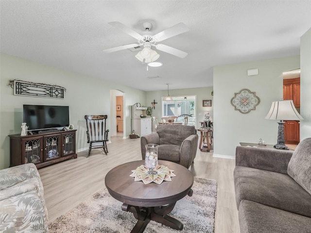 living area with arched walkways, light wood-style floors, a textured ceiling, and ceiling fan