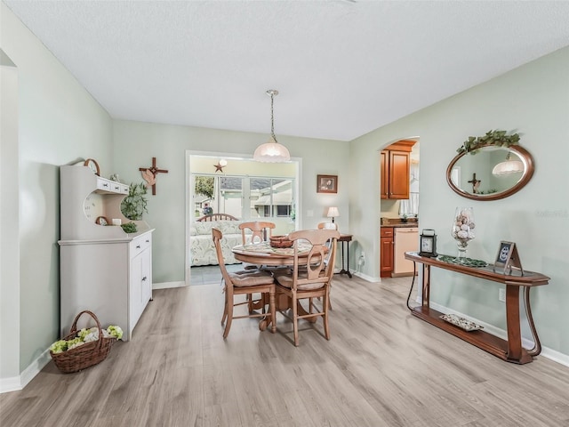 dining room featuring light wood-style flooring, arched walkways, and baseboards