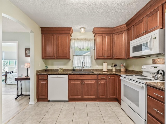 kitchen featuring white appliances, arched walkways, a textured ceiling, light tile patterned flooring, and a sink