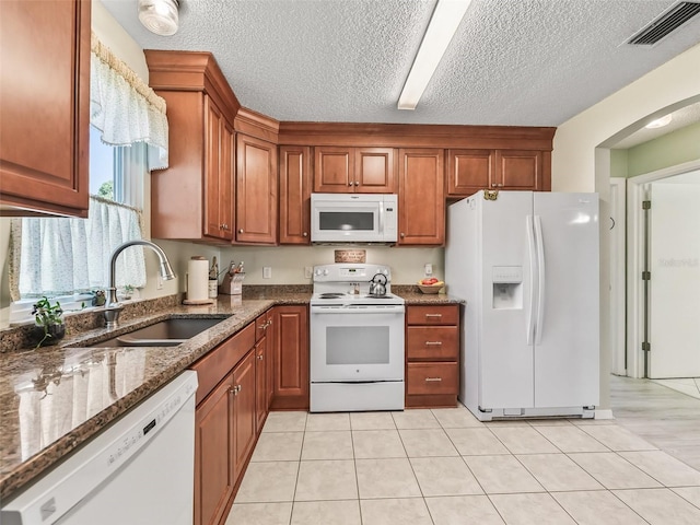 kitchen featuring white appliances, visible vents, dark stone countertops, a sink, and brown cabinets