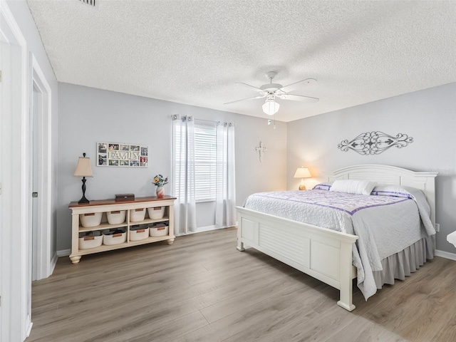 bedroom featuring ceiling fan, a textured ceiling, wood finished floors, and baseboards