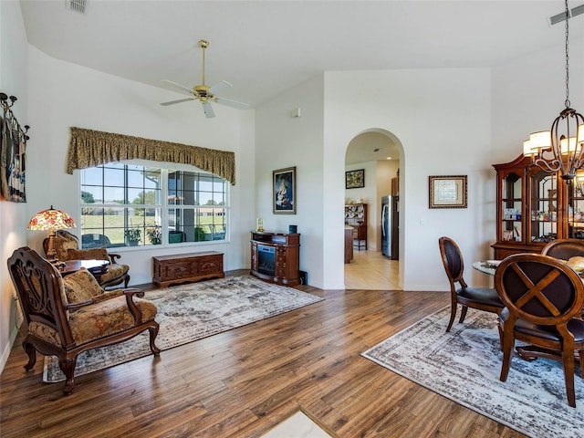 living area with visible vents, arched walkways, a high ceiling, wood finished floors, and ceiling fan with notable chandelier