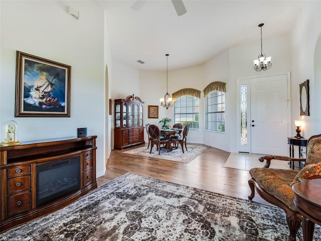 entryway featuring visible vents, a towering ceiling, wood finished floors, and ceiling fan with notable chandelier