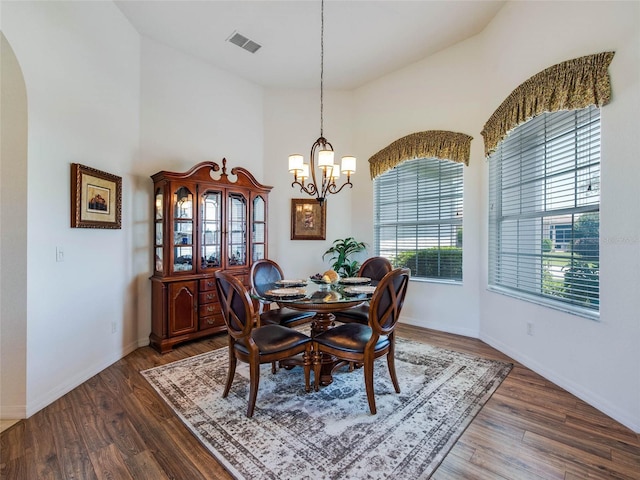 dining space featuring a towering ceiling, baseboards, a chandelier, dark wood-type flooring, and visible vents