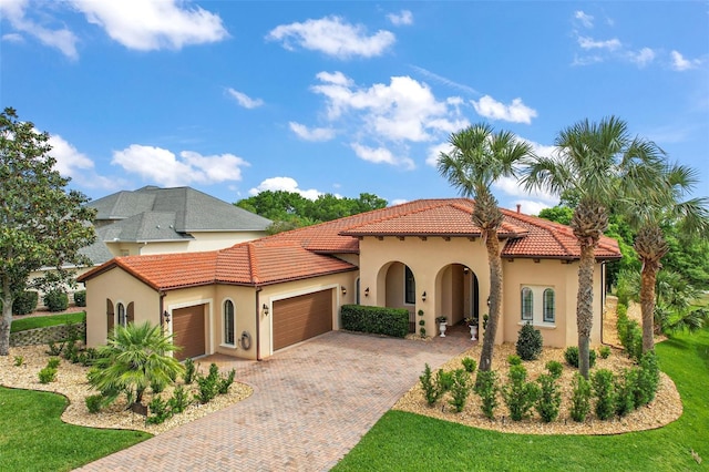 mediterranean / spanish-style home featuring stucco siding, decorative driveway, a front lawn, a tile roof, and a garage