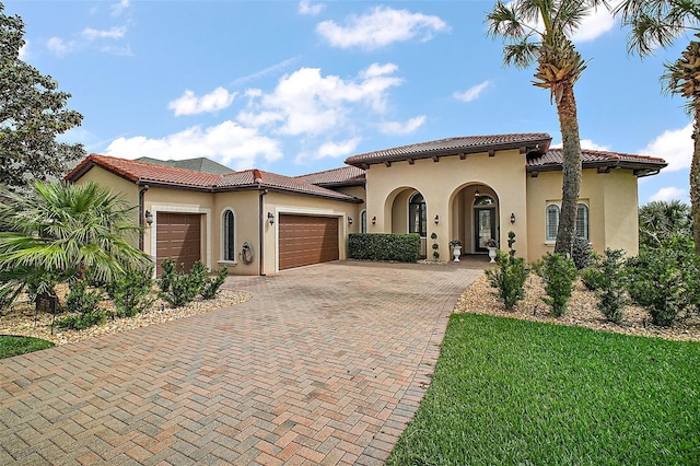 mediterranean / spanish house with a tile roof, an attached garage, decorative driveway, and stucco siding
