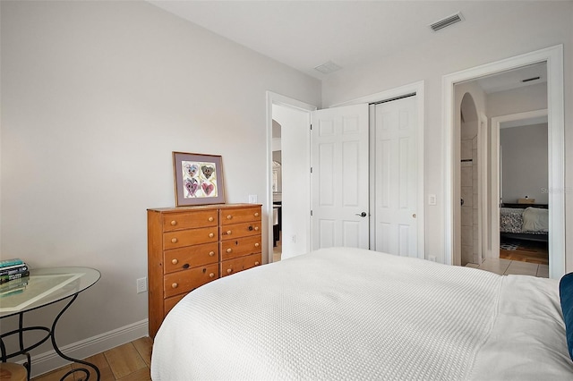 bedroom featuring arched walkways, a closet, visible vents, wood finished floors, and baseboards