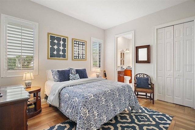 bedroom featuring light wood finished floors, ensuite bathroom, a closet, and baseboards