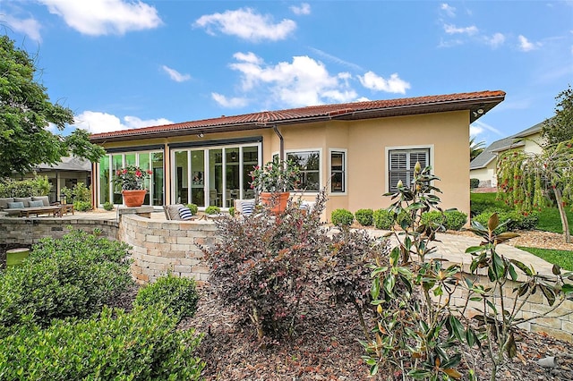 rear view of house featuring a patio, stucco siding, a sunroom, and a tile roof