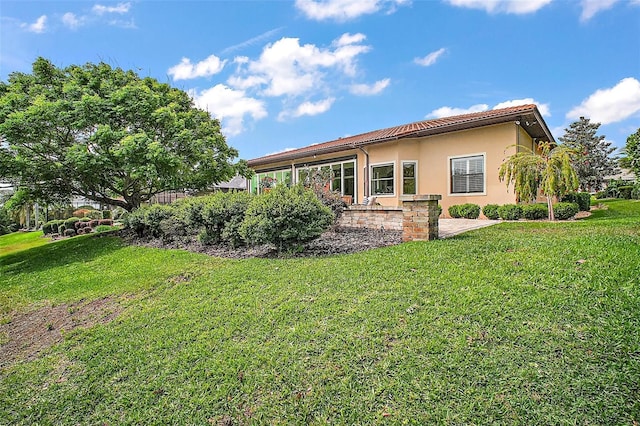 back of property with stucco siding, a tile roof, and a lawn