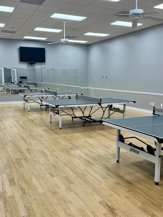recreation room featuring a ceiling fan, a drop ceiling, wood finished floors, and baseboards