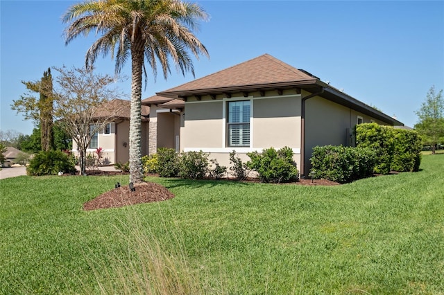 view of front facade featuring a front yard, a shingled roof, and stucco siding