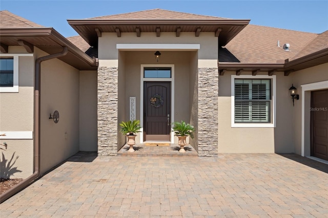entrance to property with a shingled roof, stucco siding, and stone siding