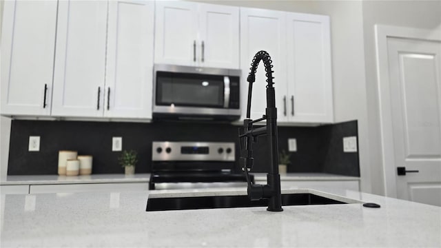 kitchen featuring white cabinets, a sink, appliances with stainless steel finishes, and light stone counters