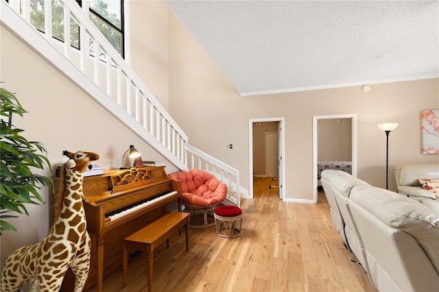 living room featuring crown molding, baseboards, stairway, a textured ceiling, and light wood finished floors