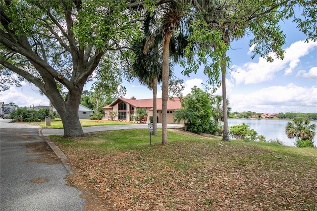 view of front of home with curved driveway, a water view, stucco siding, and a front lawn