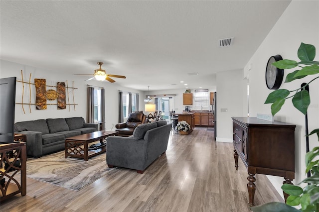 living area featuring visible vents, baseboards, a ceiling fan, and wood finished floors
