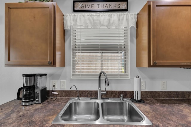 kitchen featuring brown cabinetry, a sink, and dark countertops