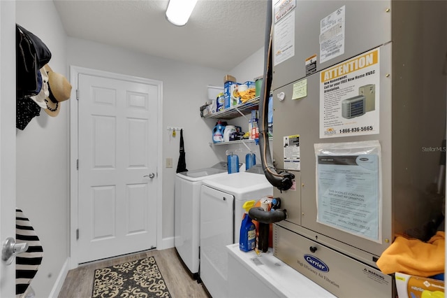 laundry area with a textured ceiling, heating unit, laundry area, light wood finished floors, and washing machine and clothes dryer