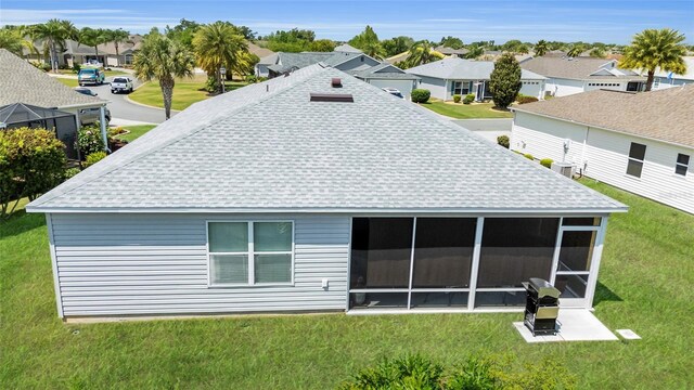 rear view of house featuring a sunroom, roof with shingles, a residential view, and a lawn