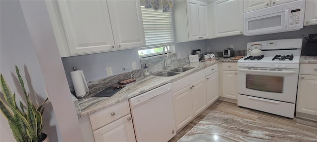 kitchen featuring white appliances, light stone countertops, white cabinets, a sink, and light wood finished floors