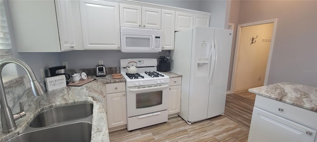 kitchen featuring white appliances, light stone countertops, light wood-type flooring, white cabinets, and a sink