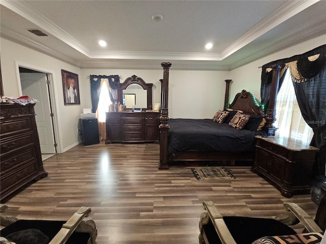 bedroom with a tray ceiling, crown molding, wood finished floors, and visible vents