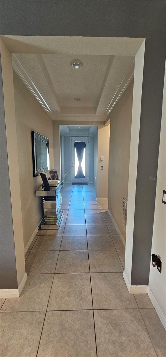 hallway featuring visible vents, baseboards, a raised ceiling, and light tile patterned flooring