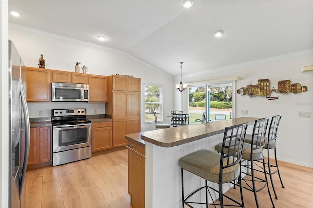 kitchen featuring vaulted ceiling, dark countertops, a breakfast bar, stainless steel appliances, and ornamental molding