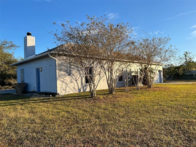 rear view of house with a chimney, a garage, a lawn, and stucco siding