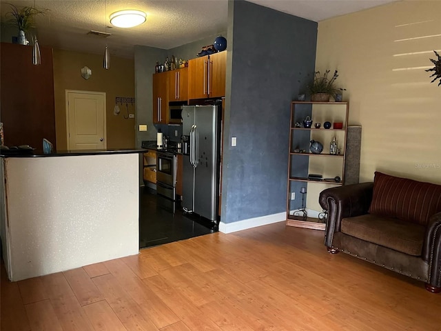 kitchen with dark countertops, visible vents, brown cabinets, appliances with stainless steel finishes, and wood finished floors