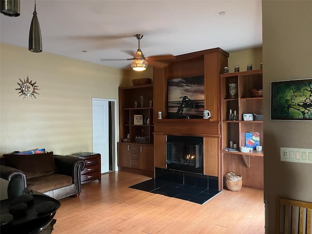 living area with a tile fireplace, ceiling fan, and wood finished floors