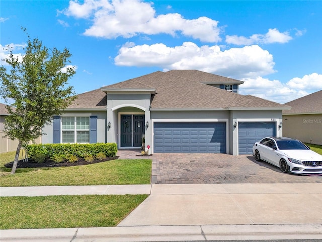 view of front of house with roof with shingles, stucco siding, driveway, a front lawn, and a garage