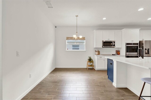 kitchen featuring white cabinets, decorative backsplash, wood finished floors, and stainless steel appliances