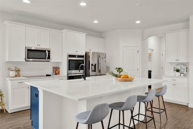 kitchen featuring arched walkways, light wood finished floors, white cabinetry, and appliances with stainless steel finishes