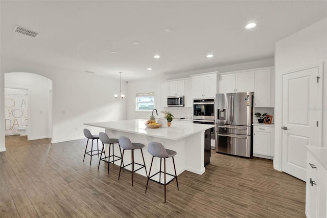 kitchen with visible vents, white cabinets, arched walkways, a center island with sink, and stainless steel appliances