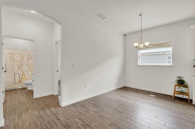 interior space with arched walkways, visible vents, wood finished floors, baseboards, and a notable chandelier