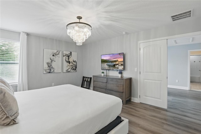 bedroom with wood finished floors, an inviting chandelier, baseboards, and visible vents