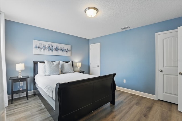 bedroom with a textured ceiling, wood finished floors, baseboards, and visible vents