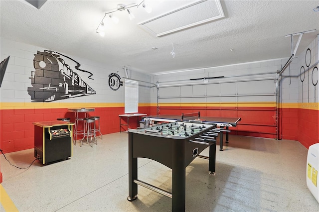 game room featuring a textured ceiling, a garage, speckled floor, and concrete block wall