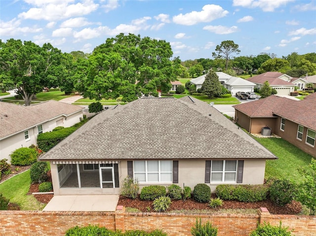 rear view of property featuring a yard, a shingled roof, and stucco siding