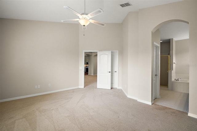 unfurnished bedroom featuring baseboards, a high ceiling, visible vents, arched walkways, and light colored carpet