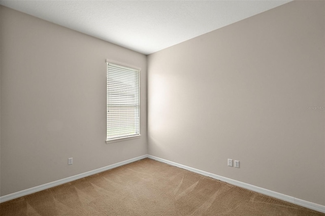 spare room featuring light carpet and baseboards