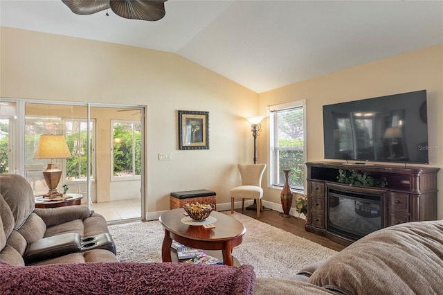 living area with a glass covered fireplace, lofted ceiling, wood finished floors, baseboards, and a ceiling fan