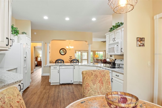 kitchen with white cabinets, an inviting chandelier, light stone counters, white appliances, and wood finished floors