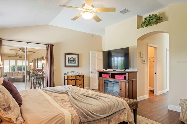 bedroom featuring visible vents, a glass covered fireplace, wood finished floors, lofted ceiling, and access to exterior