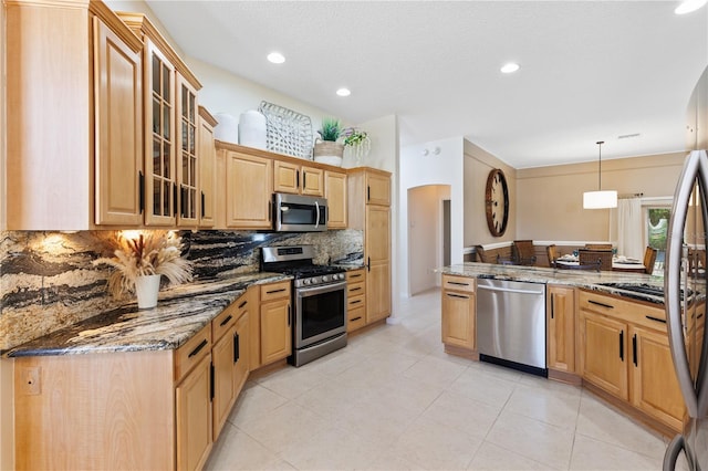 kitchen with glass insert cabinets, hanging light fixtures, stainless steel appliances, stone counters, and decorative backsplash