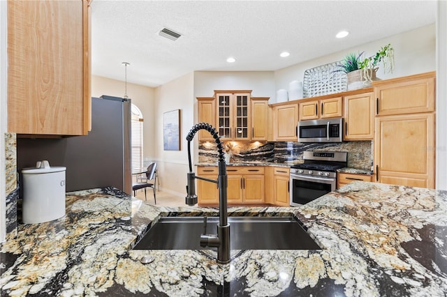 kitchen featuring tasteful backsplash, visible vents, appliances with stainless steel finishes, light stone counters, and a sink