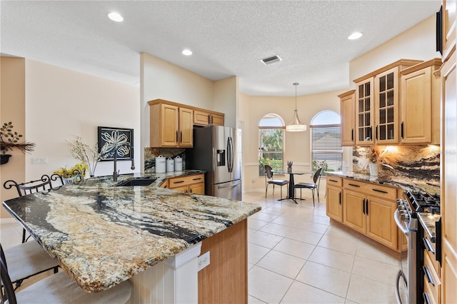 kitchen featuring a kitchen breakfast bar, a peninsula, visible vents, a sink, and stainless steel appliances